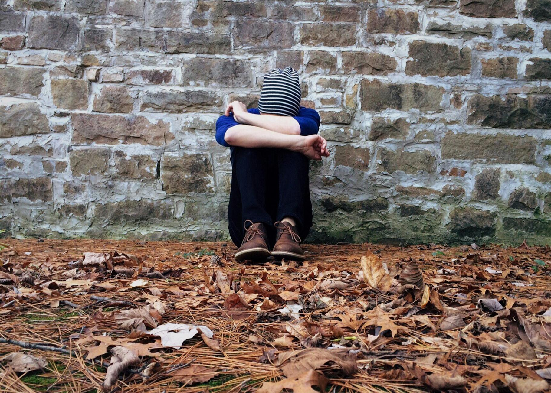 boy sitting on ground leaning against brickstone wall