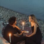 man and woman sitting on rock while holding lighted candles