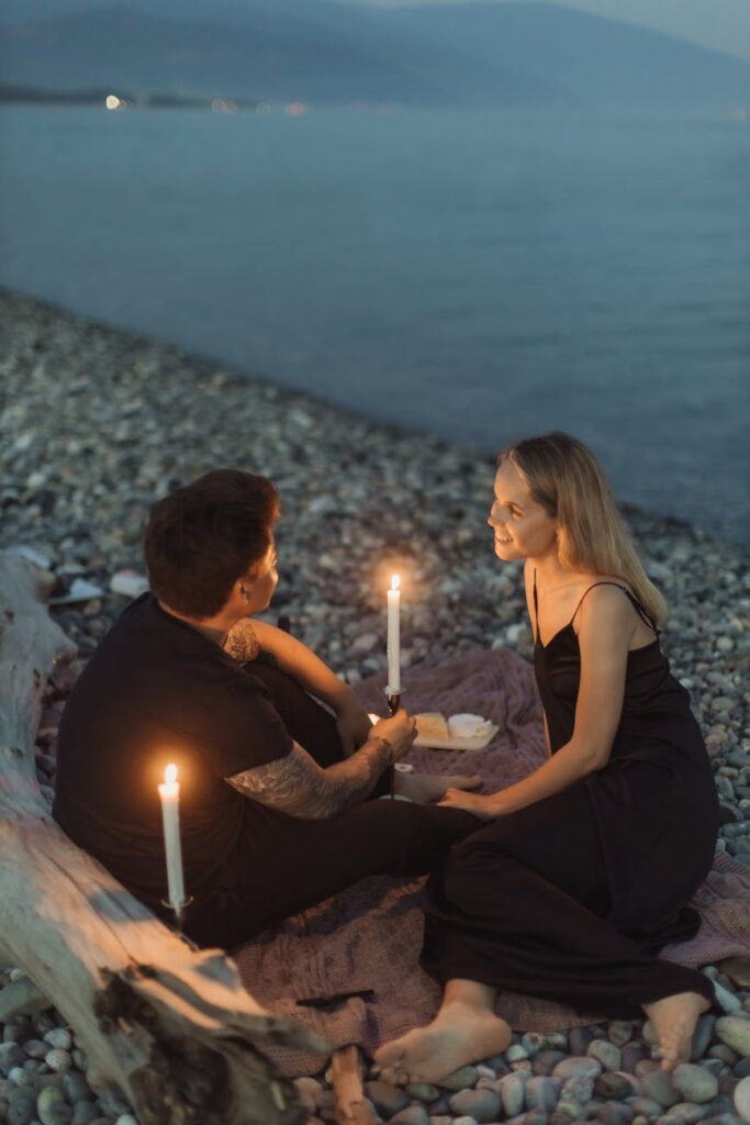 man and woman sitting on rock while holding lighted candles