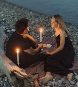 man and woman sitting on rock while holding lighted candles